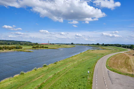 Typical Dutch river landscape with cows, grassland, floodplain, dike with road and the river Rhine...