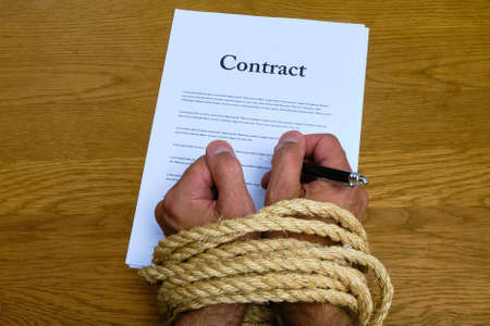 Contract and tied hands holding pen ready to sign. Bound hands while signing unfair contract. Contract limits freedom of employee.の写真素材