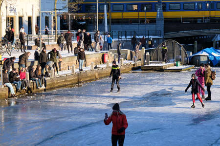 Amersfoort, Netherlands - Feb 13, 2021: Dutch police man and other people ice skating on frozen canal the Eem in city center of Amersfoort.のeditorial素材