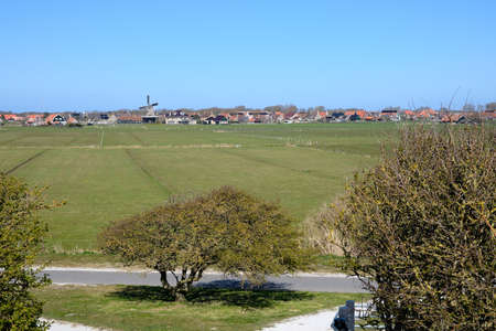 Typical Dutch picture overlooking meadow and the old Dutch village of Hollum, Ameland with a windmill on a sunny day. April 2021の写真素材