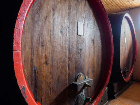 Picture of two brown wine barrels stacked in the old cellar of the winery. Background of the wooden...