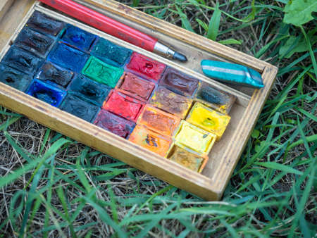 Picture of the used water colour paint laying on the green grass. Background of the colourful paint...