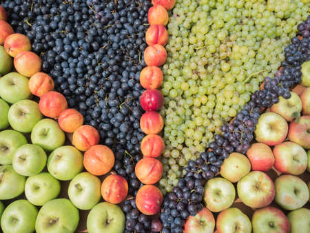 Background of fresh colourful fruits. Frame composition of fruits on market stall. Colourful fruits pattern close up. Green and red apples, orange peaches.の写真素材