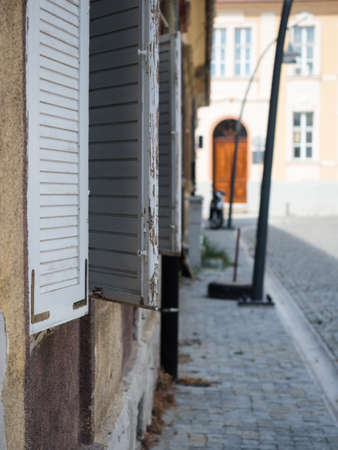 Selective focus on the window with white wooden shutters against the blurred background of another building of the street. White wooden shutters against the blurred background of the road.の写真素材