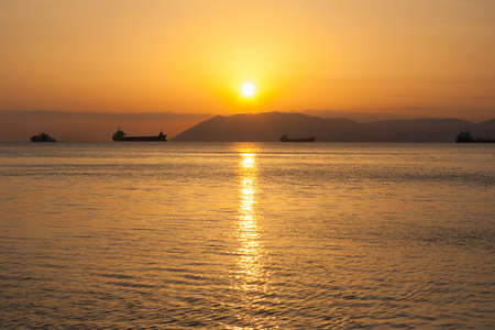 Natural summer sea sunset. Silhouettes of ships and strip of land on the horizon. Orange sea sunset in eveningの写真素材