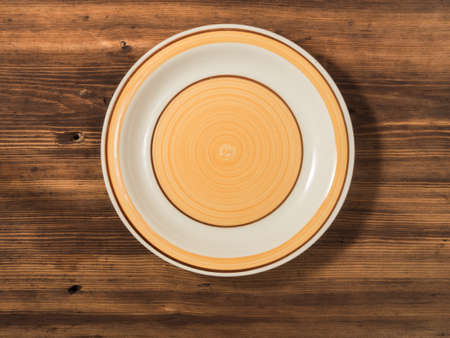 Orange round plate is photographed top view on a background of old wood table planks. Ceramic plate with round patternの写真素材