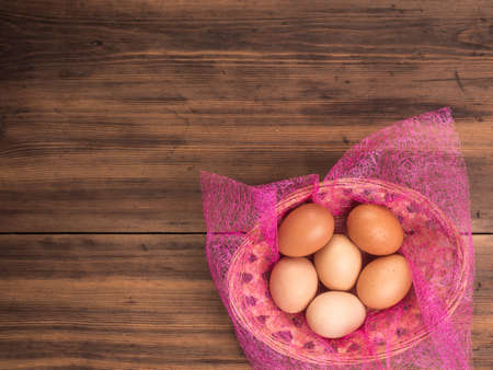 Easter eggs in the basket on the background of wooden table from the old boards, top view. Background with copy-space in rustic style for advertising or Easter greetingsの写真素材