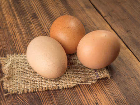 Brown chicken eggs lay on a piece of burlap on a wooden table from the old boards. Three fresh...