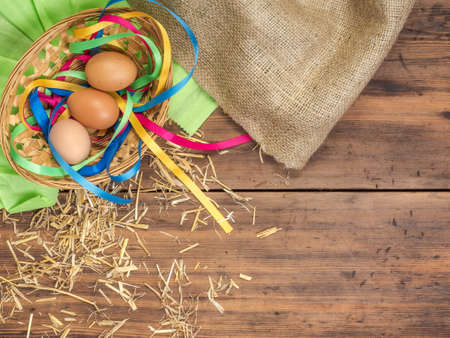 Rural eco background with brown chicken eggs, a piece of burlap, colored ribbons and straw on the background of old wooden planks. The view from the top. Creative background for Easter cards or menuの写真素材