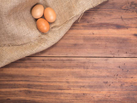 Chicken eggs on old rural wooden table boards and burlap vintage background, photo top view. Hessian, sacking texture with eggs on wooden background for design, Easter greetings card or advertisementの写真素材