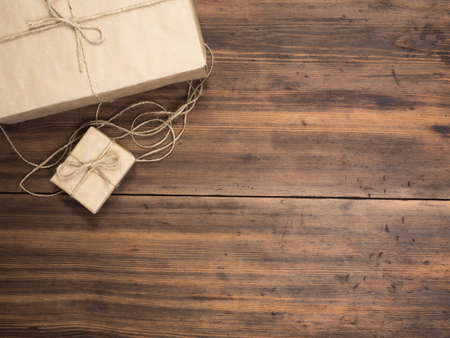 Boxes in craft paper, eco paper on the wooden table. Top view. Parcels or gifts tied with twine. Brown paper wrapped gift box with rope bow on a old rustic wood background. Background for your designの写真素材