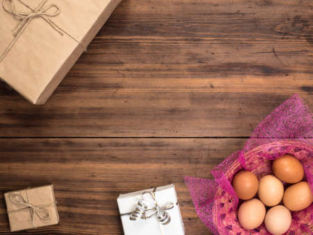 Easter eggs in the basket on the background of wooden table from the old boards with gift boxes, top...