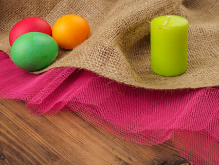 Easter colored egg with candle. Mock up for your greetings card or design. Russian and Ukrainian, orthodox, slavic traditional Easter, rural background with burlap and colored meshの写真素材