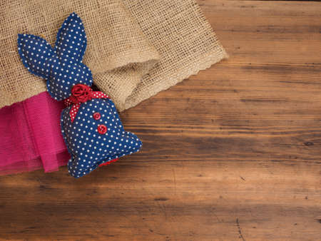Vintage, rustic background with a toy rabbit on background of burlap and old wooden table. Top view.