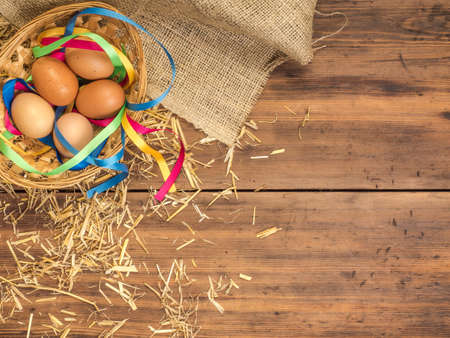 Rural eco background with brown chicken eggs, a piece of burlap, colored ribbons and straw on the background of old wooden planks. The view from the top. Creative background for Easter cards or menuの写真素材