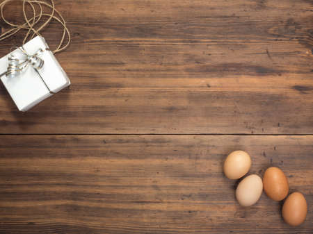 Easter eggs, gift box on old wooden table from planks. Top view with space for your design, Easter greetings or advertising. Rustic background. Composition of eggs and gift boxes tied with stringの写真素材