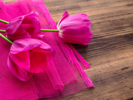 Pink tulips, floral arrangement on wooden background with pink mesh and space for message. Background for Mothers Day, 8 March and other greeting cards or invitations for lovely women. Soft focus.の写真素材
