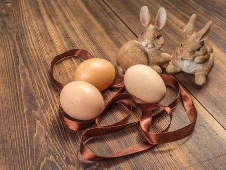 Easter bunnies on the background of wooden table from the old boards with ribbon and brown chicken eggs. Background in rustic style for advertising or Easter greetingsの写真素材