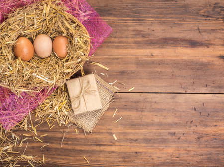 Brown eggs in hay nest. Rural eco background with brown chicken eggs and straw on the background of old wooden planks. Top view. Creative background for Easter cards, restaurant menu or designの写真素材