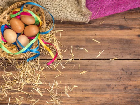 Rural eco background with brown chicken eggs, a piece of burlap, colored ribbons and straw on the background of old wooden planks. The view from the top. Creative background for Easter cards or menuの写真素材
