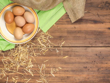 Rural eco background with brown chicken eggs, a piece of burlap and straw on the background of old...