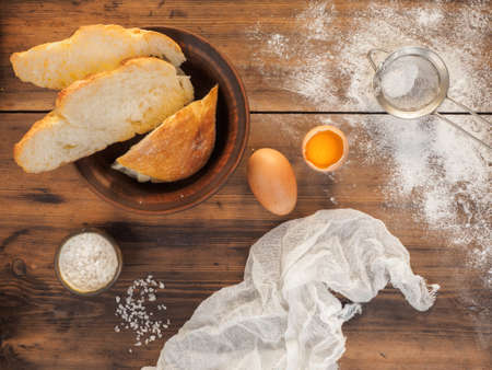 Sliced bread, scattered the flour, salt, egg yolk and tissue. Still life on the background of the old wooden table, top view in rustic style.の写真素材