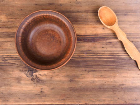 Empty clay bowl with wood spoon on old wooden table. Rural composition, top view. Template for menu, poster or print design.の写真素材