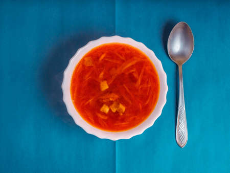 White plate with red home Ukrainian, Russian borscht on a colored background with a metal spoon. Abstract composition on the theme of food, top view. National cuisine, soup with beetroot and cabbage.の写真素材