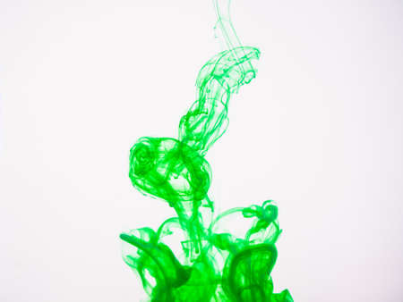 Green acrylic colour dissolving into water, close up view. Abstract green coloured background. Acrylic paint dropped into water and photographed while in motion. Droplet of color on white backgroundの写真素材