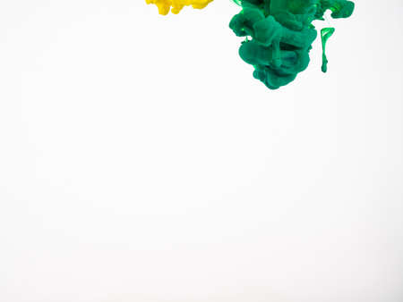 Two droplets of acrylic paint just dropped into water, isolated on white background. Yellow and green droplets of acrylic ink in water, abstract background. Yellow and green droplets of ink in waterの写真素材