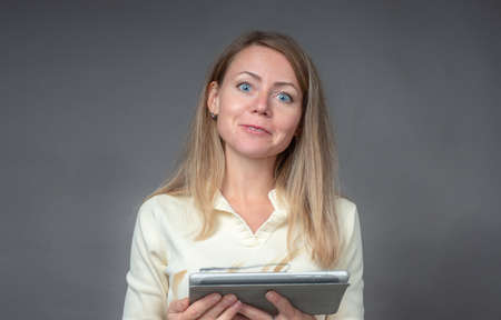 Portrait of european woman with tablet isolated on gray background. Enthusiastic young student looks directly into the camera. Businesswoman working online with digital mobile computerの写真素材