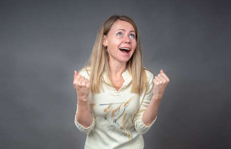 Excited brunette girl glad to achieve of goal. She clenches fists, screams in excitement with raised up head and eyes. Concept of winning, success , and achievement life goalsの写真素材