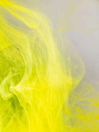 Transformation of ink droplet in water, close up view. Blurred background. Yellow paint dissolving into water, abstract pattern. Acrylic clouds in liquid, abstract background. Ink swirling in liquidの写真素材