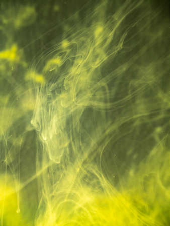 Yellow paint dissolving into liquid, close up view. Blurred background. Acrylic smoke swirling under water, abstract pattern. Paint clouds mixing with water, abstract background. Abstract artの写真素材
