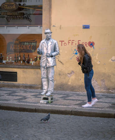 Prague, Czech republic - april 2019: Young girl observing live sculpture in street. Man as a grey live sculpture stands near shop window. Graffiti on beige wall of building in Pragueのeditorial素材