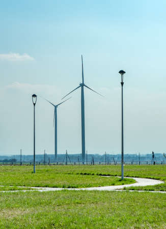 Two wind generators on green meadow. Windmachines under clear blue sky. Big wide meadow covered with...