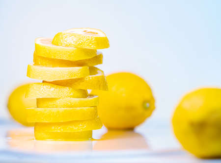 Pile of juicy slices and whole lemons, close up view. Fruit composition on light background. Yellow lemons on white table. Blurred background. Selective soft focusの写真素材