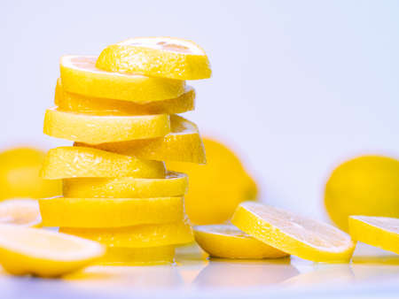 Yellow slices of lemon on light desk. Pile of juicy slices, fruits composition. Blurred background. Selective soft focusの写真素材