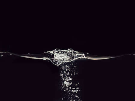 Droplet of water dropped into liquid isolated on black background, close up view. Rippling surface and bubbles underwater. Abstract background for overlays design, screen blending mode layerの写真素材