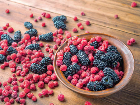 Brown basin full of red raspberries and black mulberries, close up view. Black and red berries on brown table. Fruit background. Selective soft focus. Blurred backgroundの写真素材