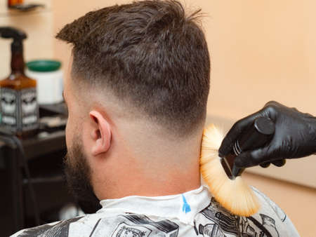 Male visiting hairdressing saloon, close up view. Stylist cutting hair with clipper. Masters hands in black rubber gloves. Interior of barbershop. Selective soft focus. Blurred backgroundの写真素材