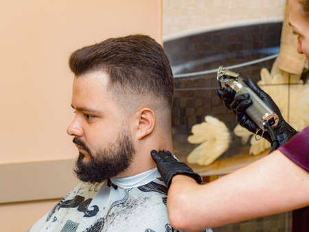 Female cutting males nape with clipper, close up view. Stylists hands in black rubber gloves....
