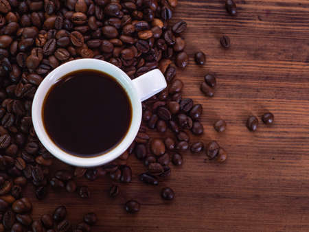 Top view on white coffee cup full of black espresso and coffee beans pilled on brown table, close...