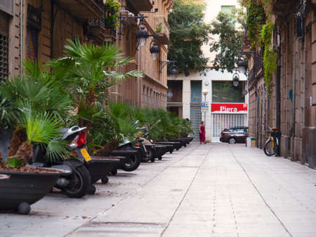 Barcelona, Spain - august 2019: bikes parking between green plants, middle view. Pavement between buildings. Female walking the street, car driving. Selective soft focus. Blurred backgroundのeditorial素材