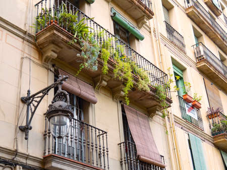 Barcelona, Spain - august 2019: beige building in city center, middle view. Green plants on balconies with black railings. Vintage lighting on wall. Selective soft focus. Blurred backgroundのeditorial素材