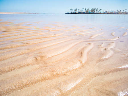 Close up view on Red Sea shallow. An abstract pattern on yellow sand. Green palm trees on horizon....