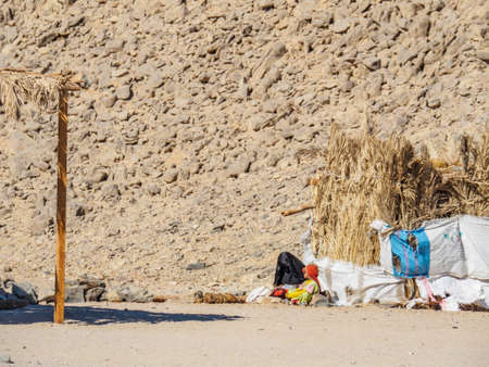 Bedouin village in desert, Egypt - February 2020: woman in black nikab and small kid sitting near...