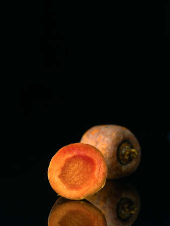 View to the cut raw carrot. Black background with reflection. Two part of carrot. Low key technique. Raw vegetablesの写真素材