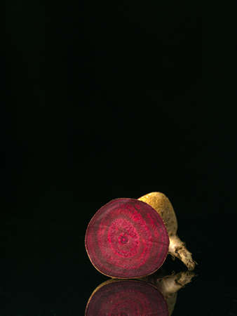 View to the cut raw beetroot. Black background with reflection. Raw vegetables. Low key technique. Vertically standing vegetable.の写真素材