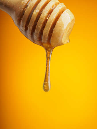 Wooden spoon with natural honey on yellow background. Drop of honey hangs from the spoon. Vertical...
